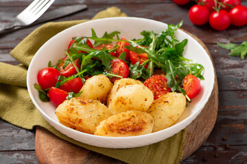 Baked potatoes and salad in a plate on a dark wooden background. Tasty rustic lunch or dinner, vegan food. Baked potatoes with tomatoes, arugula, and spices.
