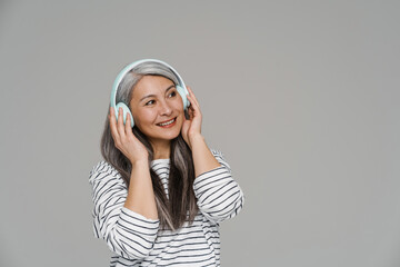 Mature white-haired woman smiling while listening music with headphones