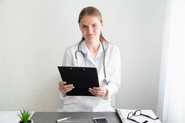 Woman doctor in an office with clipboard. Healthcare specialist at the table. Authentic people