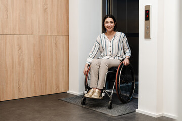 White young woman smiling while sitting in wheelchair by elevator