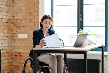 White young woman in wheelchair working with papers and laptop
