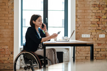 Smiling woman in wheelchair talking on cellphone and holding credit card