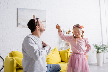 man in toy crown holding hands on chest while inviting cheerful daughter to dance