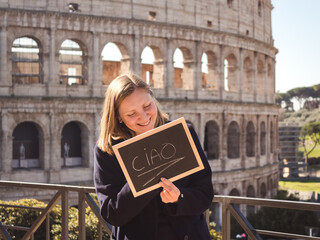 Young woman holding a sign with the inscription Ciao in Italian near the Colosseum in Rome