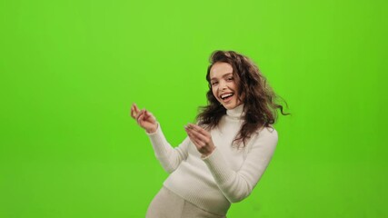 The woman is standing and looking at the camera. She is snapping her fingers and dancing. She is smiling. She is standing on a green background. Green screen. 4K - Powered by Adobe