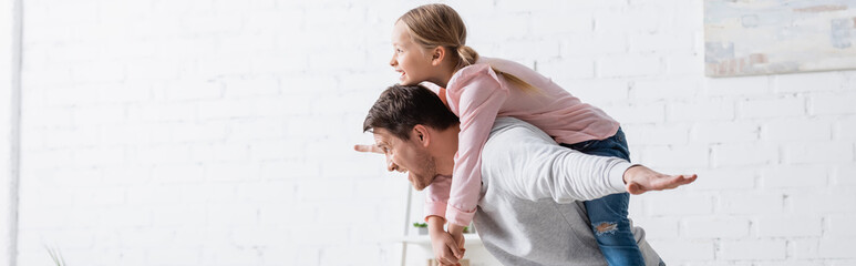 side view of man piggybacking excited daughter at home, banner