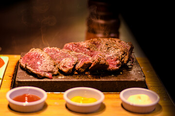 freshly cut piece of steak on the hot stone with sauces and side salad