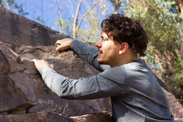 Young man climbing rock mountain on sunny day. Outdoor workout, summer hiking adventure concepts