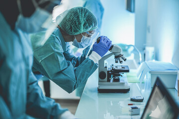 Scentist people working inside laboratory with microscope and laptop while wearing hazmat suit and...