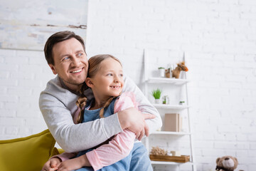smiling man looking away while embracing daughter at home