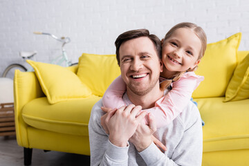 adult man laughing while cheerful daughter hugging him at home