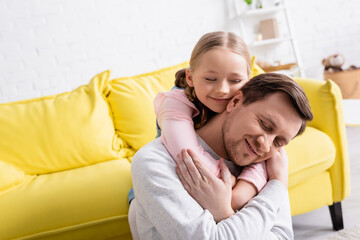Obraz premium happy father and daughter with closed eyes embracing at home