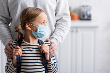 schoolgirl in protective mask looking away near father