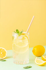 Tall glass of ice tea or water with ice cubes, lemon and mint leaves on a combined colored yellow...