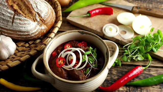 Closeup dolly shot of traditional Hungarian beef goulash with garlic, bread and paprika, garnished with chopped onion and fresh marjoram.  4K UHD video, dolly side pan.