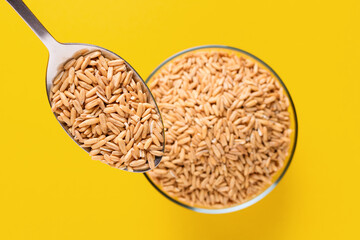 Spoon with grain Oat groats on a yellow background. Oat groats in a glass bowl. Raw whole oat seeds. Colorful. Healthy eating.