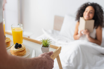 cropped view of man holding tray with tasty breakfast near happy african american girlfriend on...