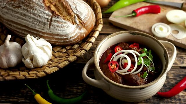 Detail of traditional Hungarian beef goulash with garlic, bread and paprika, garnished with chopped onion and fresh marjoram.  4K UHD video, dolly side pan.