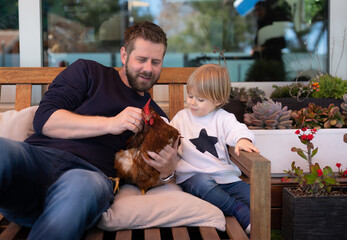 Father and son having fun together holding a chicken in the garden