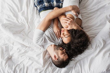top view of multiethnic couple embracing and lying on bed