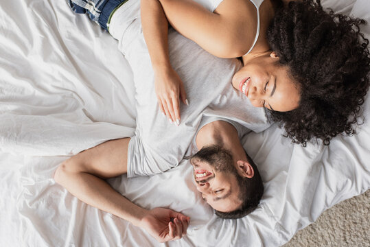 top view of smiling multiethnic couple lying on bed