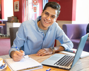 Young businessman writes something important about the project in a notebook, a working laptop is standing next to him