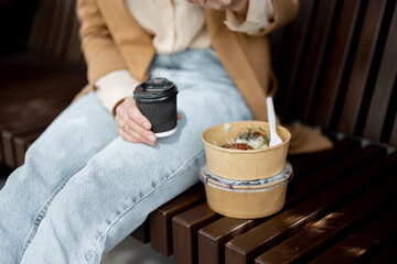 Pretty woman have outdoor lunch near office building while sitting on the bench. Healthy meal and coffee for takeaway for workers. Close up