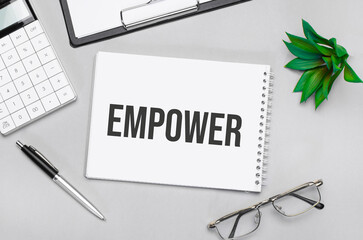 Writing text showing empower. Calculator,pen,plan,glasses and black folder on grey background