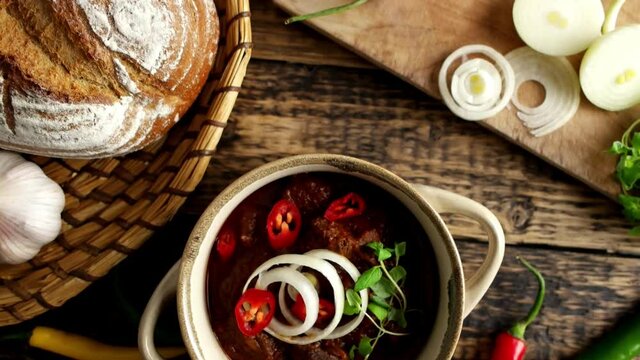 Traditional Hungarian beef goulash with garlic, bread and paprika, garnished with chopped onion and fresh marjoram.  4K UHD video, dolly side pan.