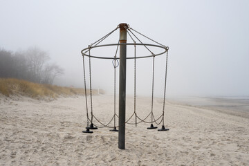 empty and broken swing on the beach with sea fog, corona lockdown, loneliness, alone, where are the kids