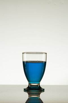 Vertical Shot Of A Glass Of Blue Drink Isolated On A Reflective Surface