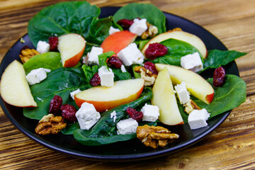 Autumn spinach salad with apple, feta cheese, walnut and dried cranberry on wooden table. Healthy vegetarian food