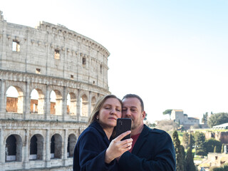 Fototapeta na wymiar Couple of young people is taking a selfie near the Colosseum in Rome, Italy