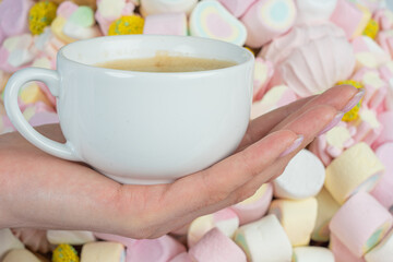 Woman's hand with a cup of coffee on the background of marshmallows, close-up.Holiday concept, congratulations.