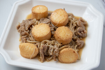Golden needle mushroom stir-fried with pork and fried tofu in white plate