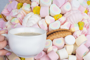 Woman's hand with a cup of coffee on the background of marshmallows, close-up.Holiday concept, congratulations.