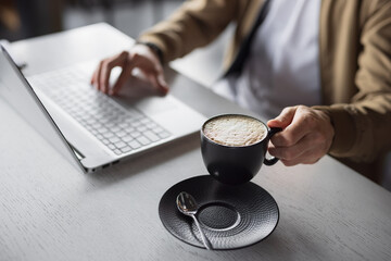 Fototapeta na wymiar Closeup male hands working on laptop keyboard take a cup of latte