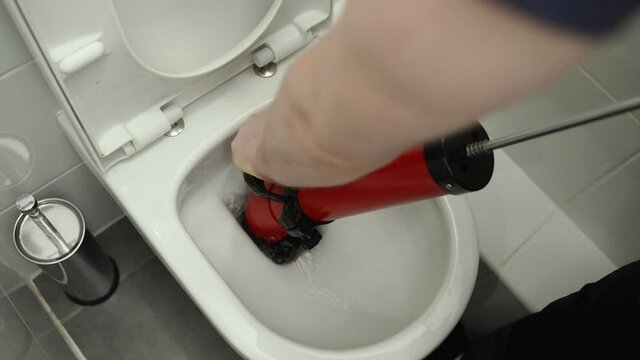 Plumber unclogging toilet with professional force pump cleaner.