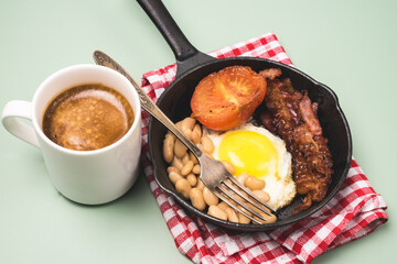 English Breakfast Fried egg Beans Tomatoes Bacon Served in Frying Pan and Cup of Black Coffee Light Green Background Copy Space