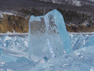 A block of transparent ice of Lake Baikal on the background of the forest. Siberia Russia