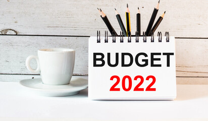 The words BUDGET 2022 is written in a white notepad near a white cup of coffee on a light background