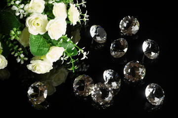 Several excellent pure diamonds and bouquet of white roses with reflection on black mirror background close up view. Jewelry diamonds sale, invitation, action, discount banner, poster template