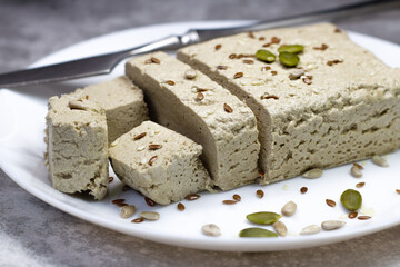 Halva close up on a white plate on a gray background. Traditional oriental dessert candy halva. Halva made from sunflower seeds. Side view.