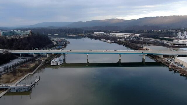 Three bridges cross the Tennessee River in Chattanooga, TN, USA. Trucks, cars and trains cross a calm smooth river using bridges connecting town on each side. Aerial view from drone over water.