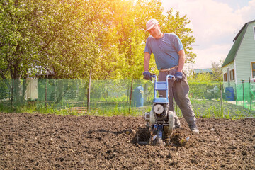 A man cultivates the soil in the garden using a motor cultivator - tiller