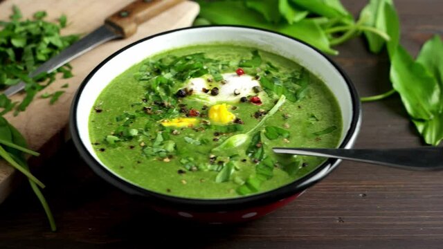 Wild garlic soup with poached egg and chopped wild garlic leaves in the backgound. 4K UHD video, dolly side pan.