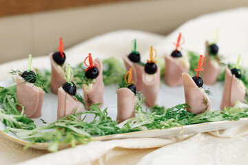 Snack for a banquet or buffet. Skewered canapes of ham, cheese and olives on a white platter,...