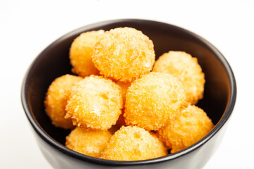 Cheese balls in a black bowl isolated on white from above. Puffed golden cheese balls as classic kids snack on wooden background