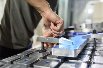 a man puts an aluminum piece on a cnc machine and prepares a processing machine..