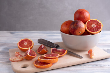 Sliced blood oranges on a cutting board with a bowl of citrus fruits on a gray background.